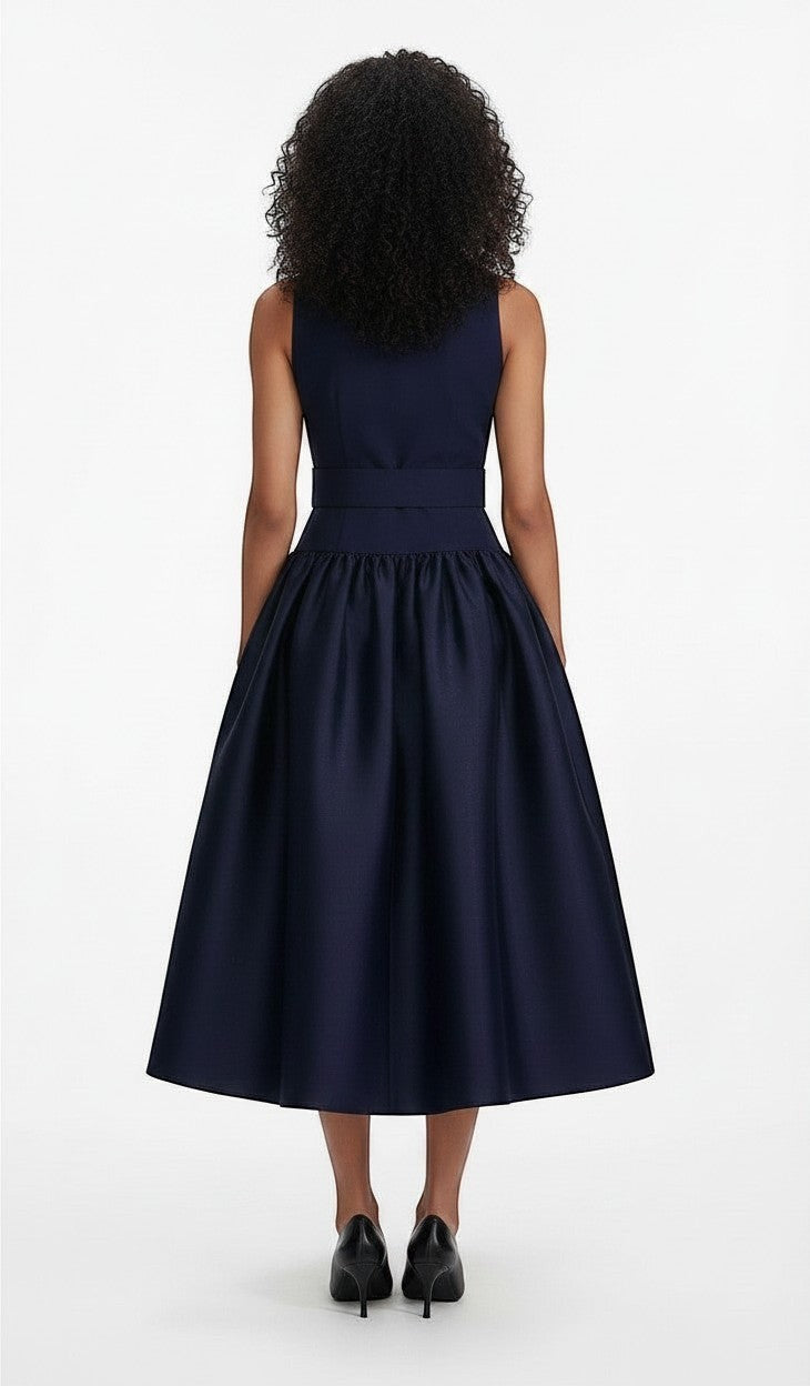 Back view of a model wearing a navy S T Y L E L I B R A R Y sleeveless midi dress with a belted waist and full skirt.