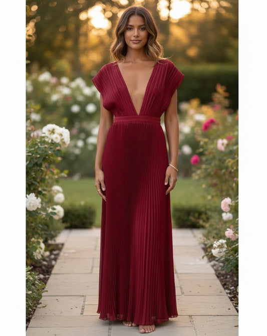 S T Y L E L I B R A R Y ruby red pleated maxi gown with a plunging neckline worn by a model in a garden setting.